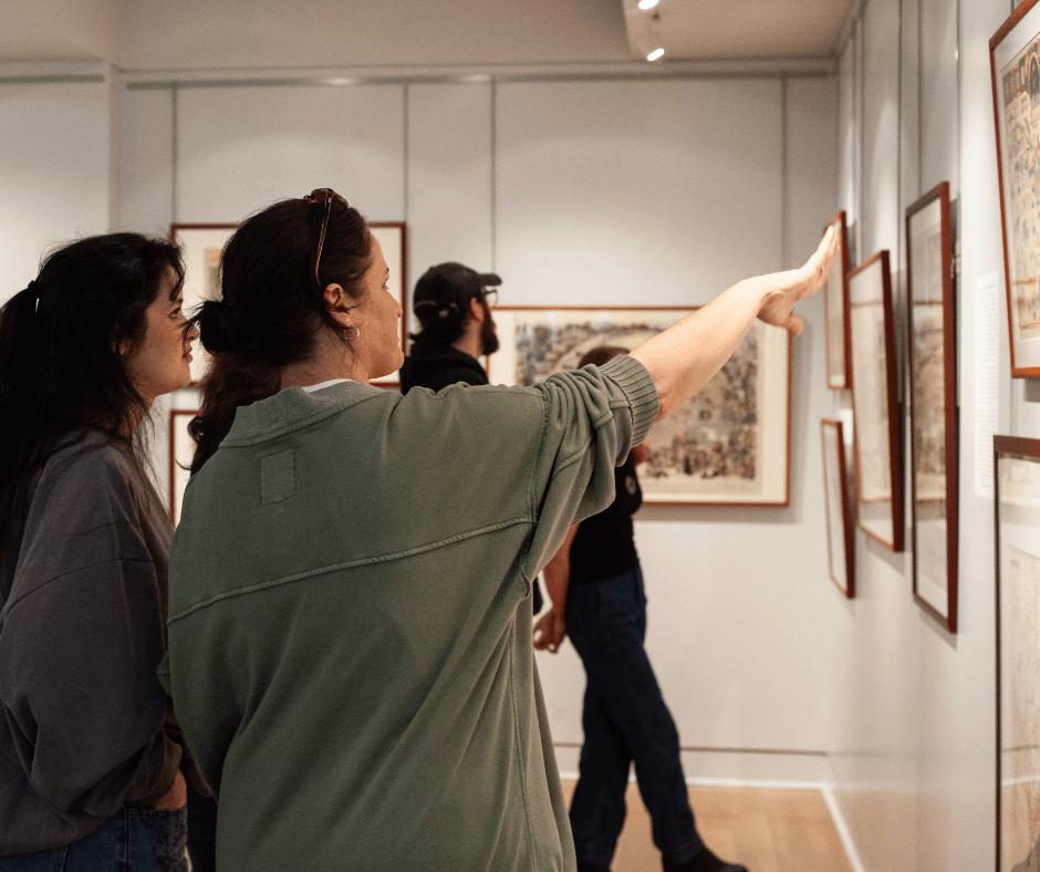 People in a gallery gesture towards framed items on the wall.